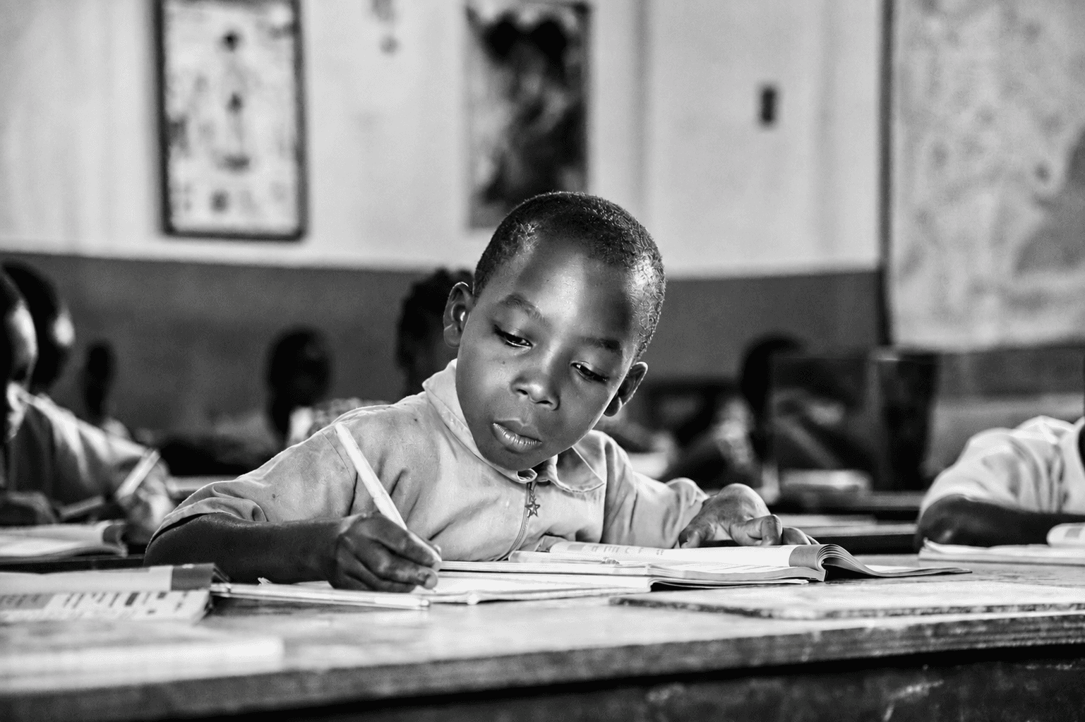 A primary-school boy writing in a notebook at his desk